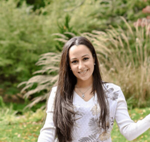 Dr. Anjelika Marti, DMD, smiling outdoors in a white floral top, standing in front of greenery in Collegeville, PA