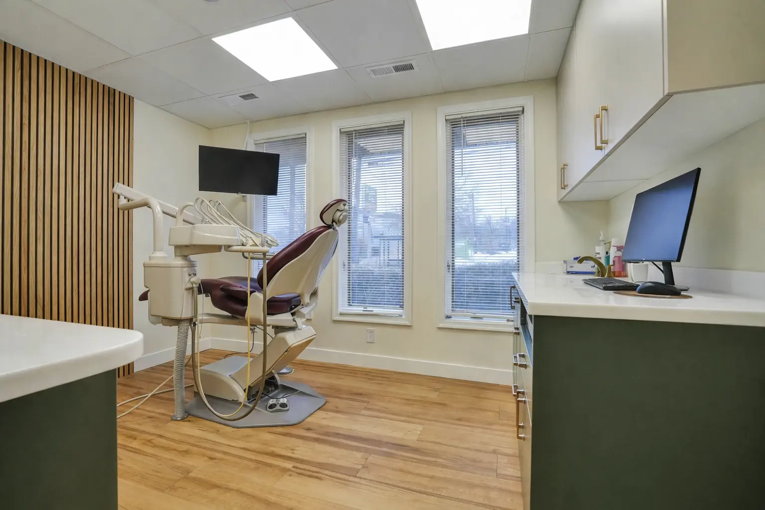 Modern dental treatment room with exam chair, computer monitor, wood flooring, and natural light at Main Street Dental Center`